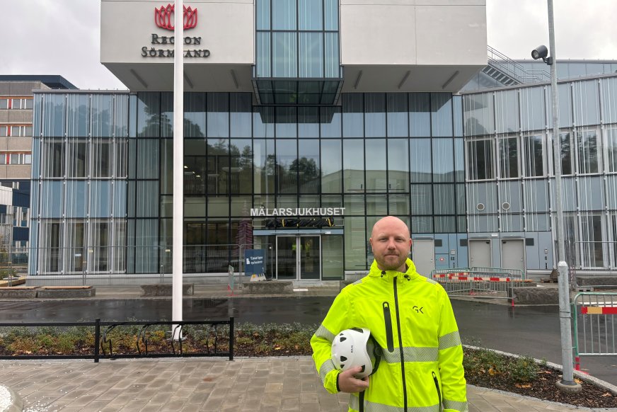 Man i varselkläder står framför sjukhusbyggnad.