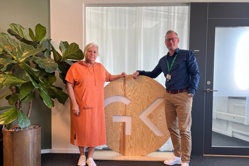Två personer står framför en skylt inomhus.