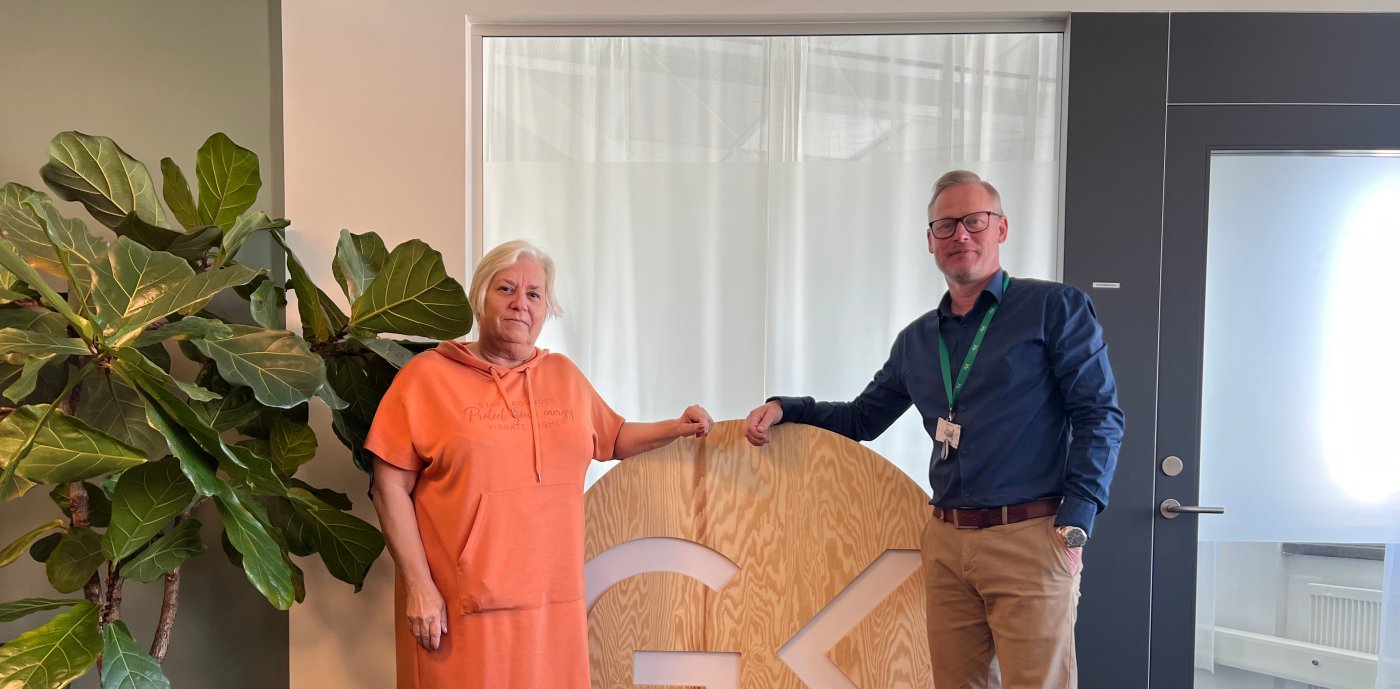 Två personer står framför en skylt inomhus.