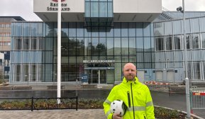 Man i varselkläder står framför sjukhusbyggnad.